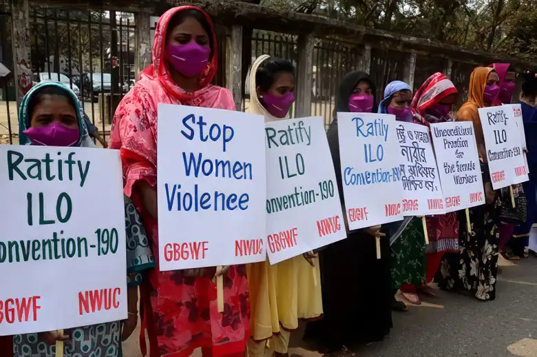 زنان معترض با پوشش سنتی و ماسک‌های بنفش که در صف ایستاده و پلاکاردهایی در دست دارند با مضمون توقف خشونت علیه زنان و تصویب کنوانسیون ۱۹۰ سازمان بین‌المللی کار (ILO).