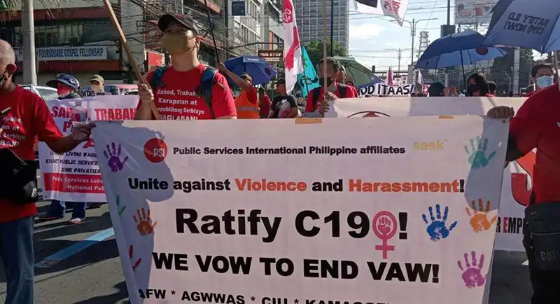 تعدادی از معترضان در خیابان که پلاکاردی با شعار «اتحاد علیه خشونت و آزار» و درخواست تصویب کنوانسیون C190 سازمان بین‌المللی کار به همراه نمادهای رنگی کف دست و نماد زنان در دست دارند.