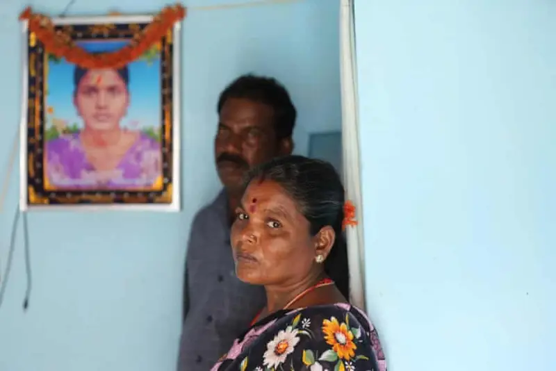 Woman and man standing inside a room with a framed photo decorated with flowers on the wall behind them.