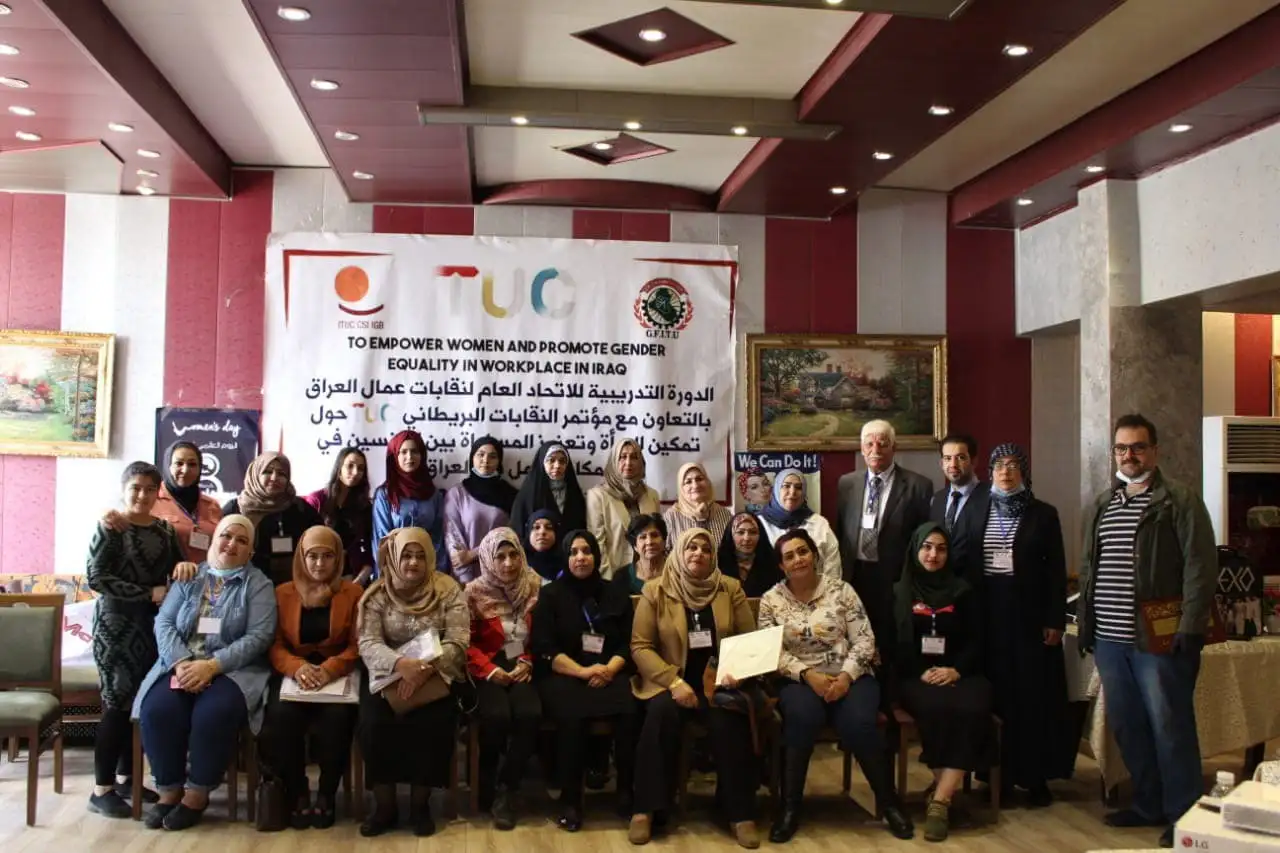 Group photo of men and women posing indoors in front of a banner that reads "To empower women and promote gender equality in workplace in Iraq."