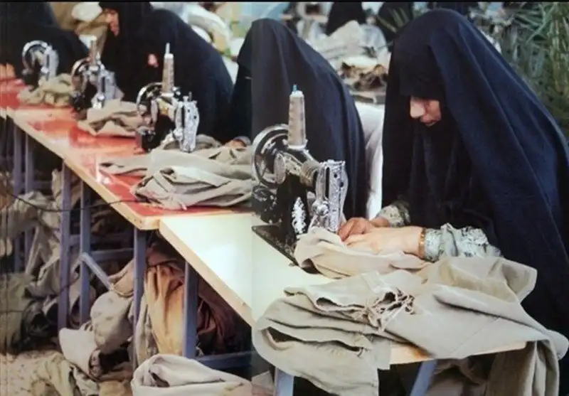 Women wearing black veils working attentively on sewing machines in a garment workshop.  