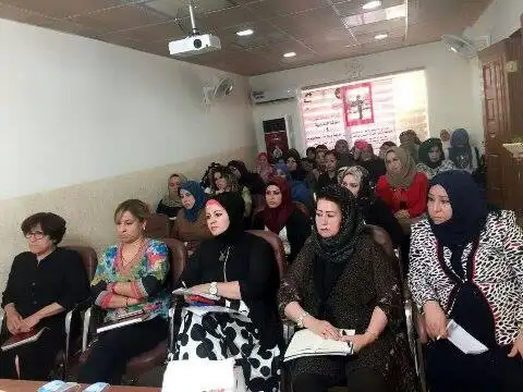 Group of women seated attentively in a classroom or meeting room, some wearing headscarves, taking notes during a session.